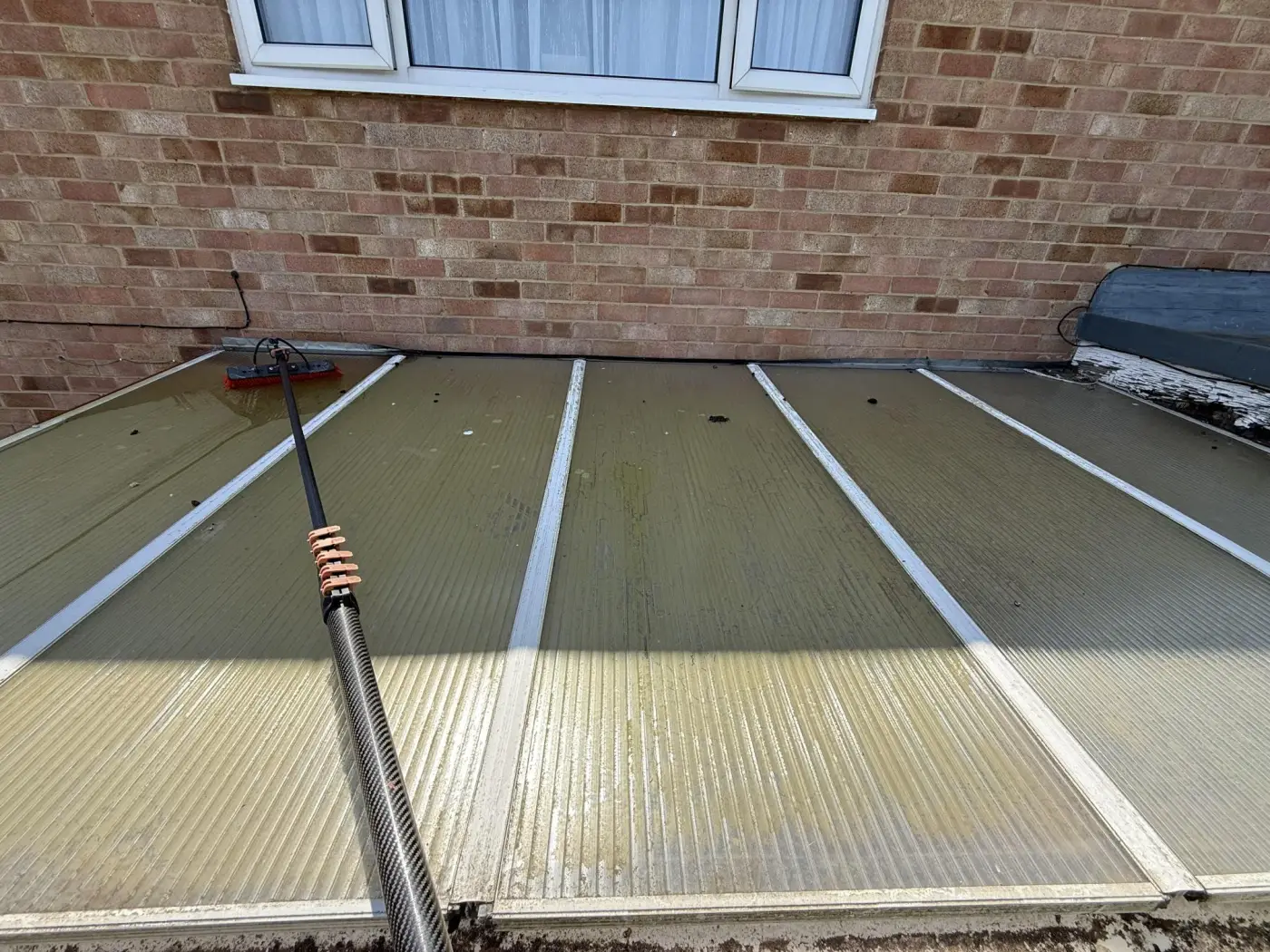 Polycarbonate conservatory roof being cleaned with a water-fed brush