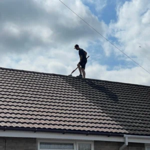 Window cleaner brushing dirt from a tiled residential roof