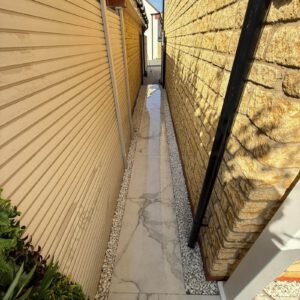 Narrow paved side passage between rendered cladding and a stone wall