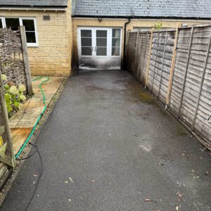 Paved driveway leading to white-framed patio doors beside a garden fence