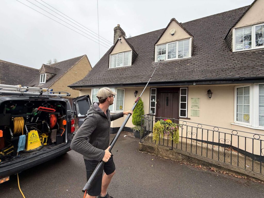 Window cleaner using an extended pole on dormer windows at a private dental practice in Painswick